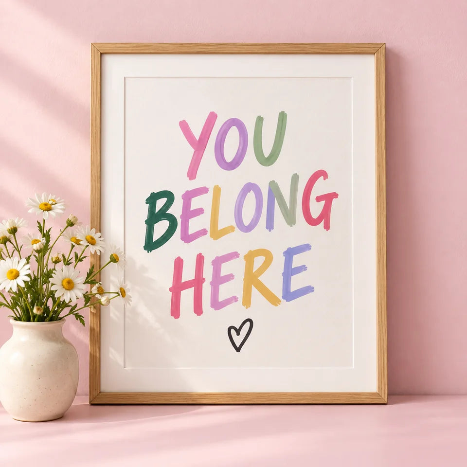 Colorful You Belong Here lettering in an oak frame on a dusty pink shelf