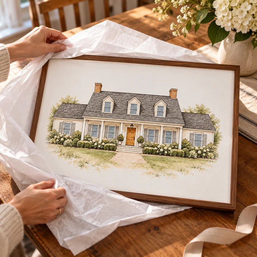 Framed Cape Cod house illustration being unwrapped on a dining table